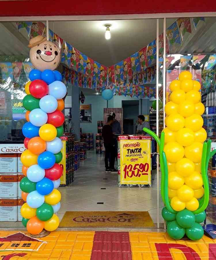 Vitrine com balões formando espantalho e milho gigantes na vitrine, além de bandeirinhas com desenho de caipiria penduradas por toda loja