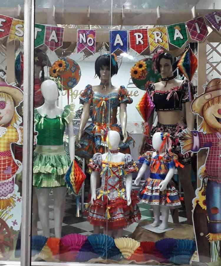 Vitrine junina com bandeirinhas, balões e manequins usando vestido típico da festa