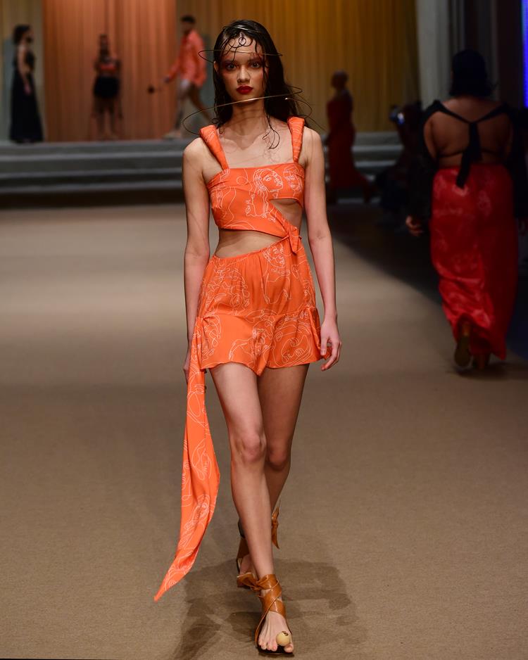 modelo em passarela com peças laranjas, vestido curto de alça