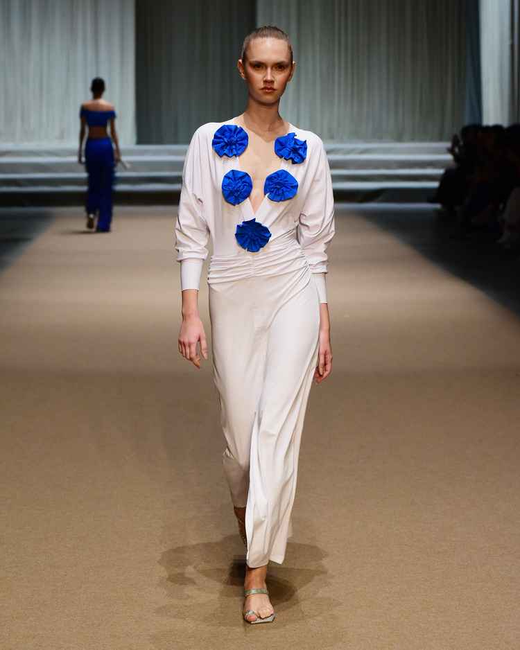 modelo em passarela com conjunto de calça e blusa branca, flores azuis na blusa