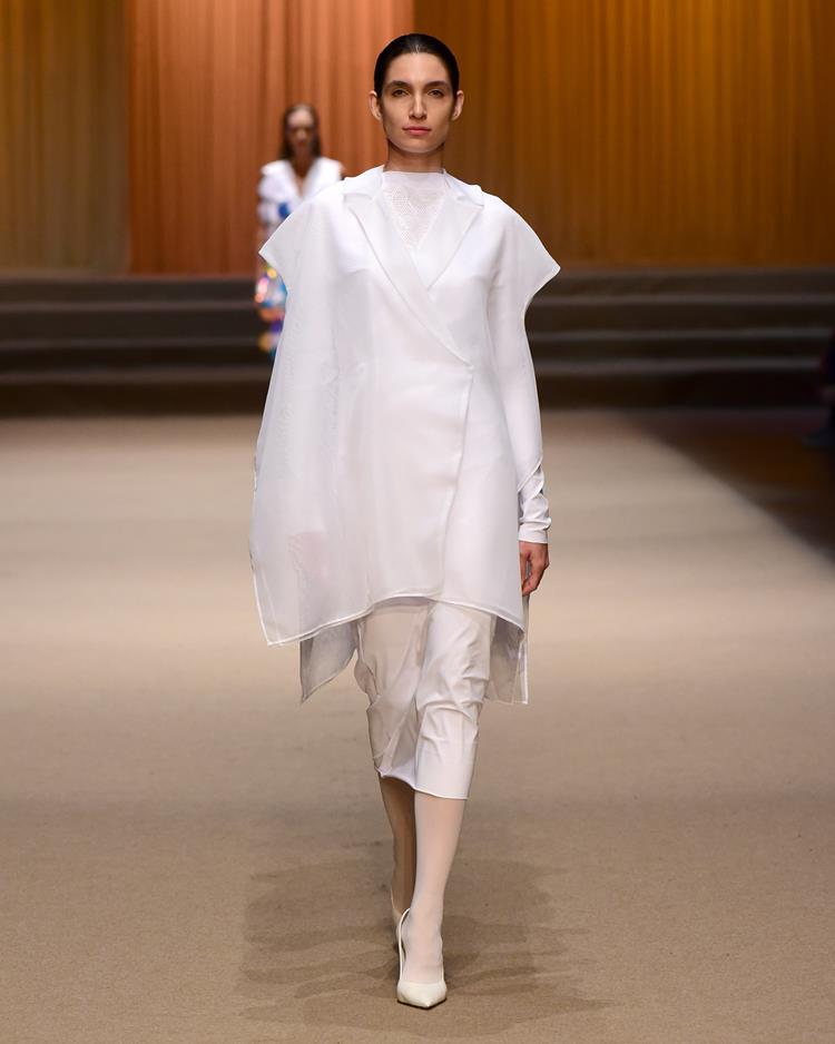 modelo em passarela com blusa branca alongada e calça curta de mesma cor
