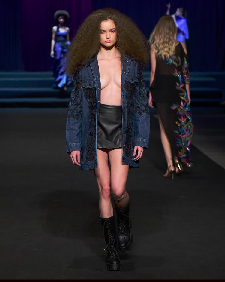 modelo em passarela com jaqueta azul marinho aberta e saia de couro preta
