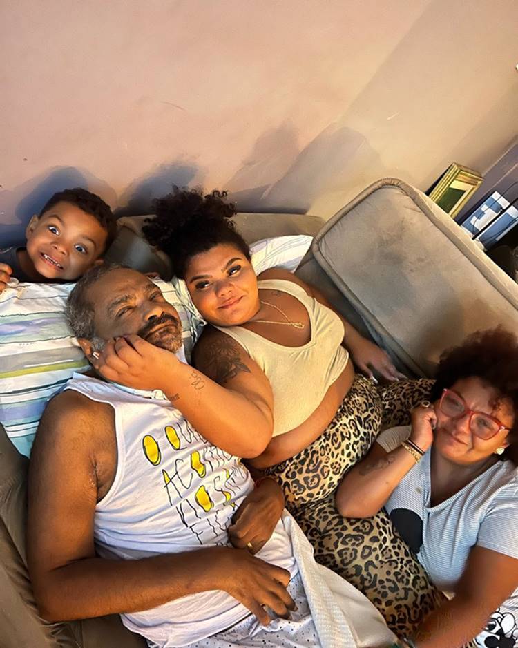 Cantor Arlindo Cruz, após AVC, deitado em sofá, com a filha Flora, a esposa Babi Cruz e o neto