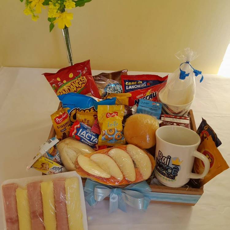 Uma cesta de café da manhã com um mimo especial, uma caneca de Dia dos Pais, recheada com salgadinhos, nescau, bolos, pastéis, café, pão, frios e outros.