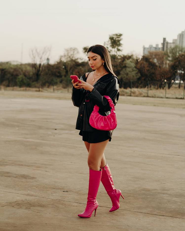 Mulher com look preto + bota pink + bolsa pink + celular pink