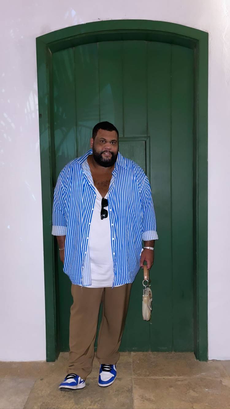 John Dropes, influenciador digital, no São João da Thay 2023: usando camisa listrada azul + camiseta branca + calça marrom + tênis azul da nike