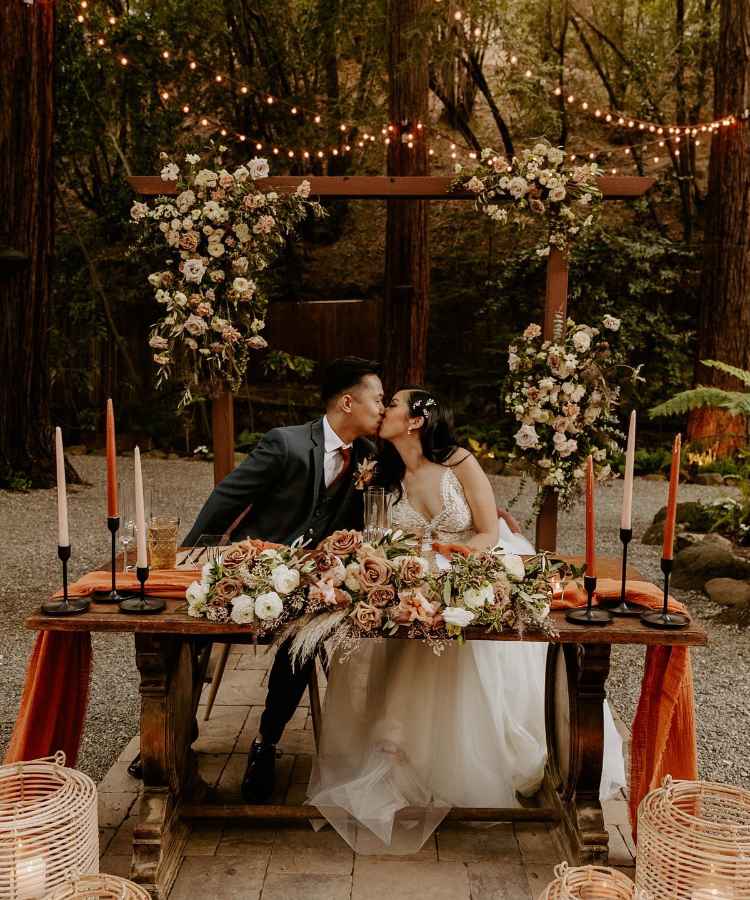 Noivos sentados em mesa decorada com flores, velas, luzes em cerimônia íntima em reserva natural