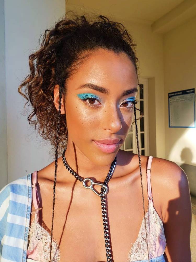 Yara Cahrry de maquiagem azul, sardas e cabelo semi preso, com tranças finas na franja 