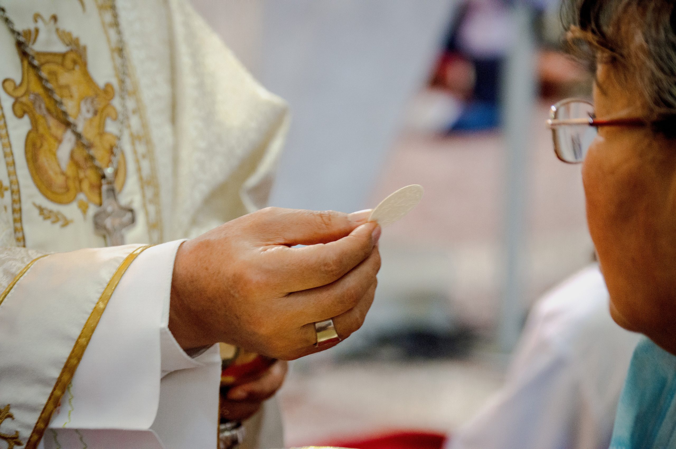 Padre entregando a hóstia (símbolo da eucaristia, comemorada no Corpus Christi) para uma senhora na igreja