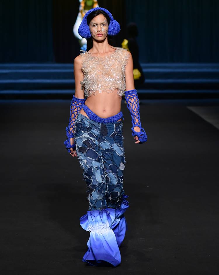 Modelo com cropped transparente, luvas de crochê azul + calça jeans + fone de crochê azul no desfile da UFCA no Dragon Fashion Brasil 2023