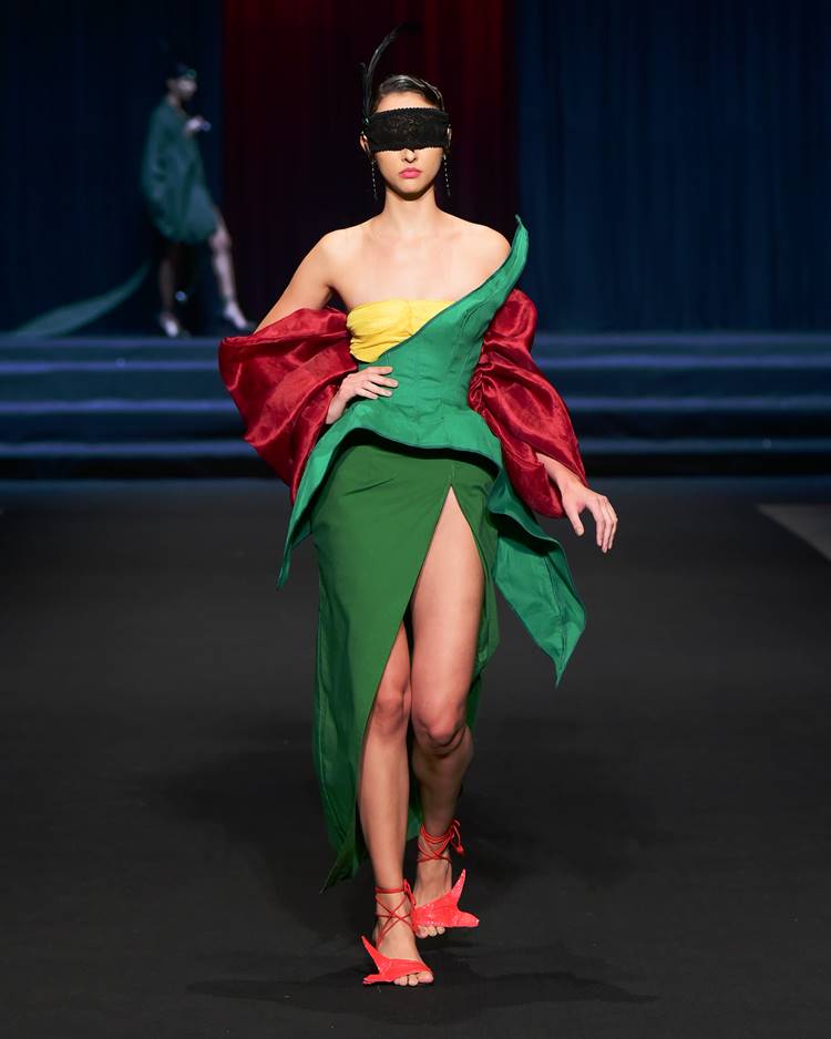 Modelo com vestido verde, amarelo e vermelho + máscara de renda nos olhos no desfile da UFMG no DFB Festival 2023