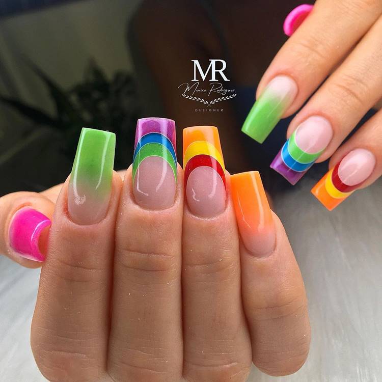 Mão com unhas arco-íris LGBTQIA+:  Polegar: nude com pink Indicador: 3 cores do arco-íris nude com verde Médio: outras 3 cores do arco-íris Anelar: Mínimo nude com laranja