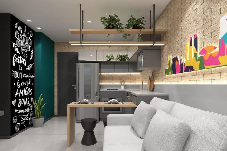 Studio com parede verde, parede preta com escritos em branco, sofá cinza, sala integrada com cozinha, plantas em prateleira e iluminação indireta, além de mesmo piso na sala e na cozinha