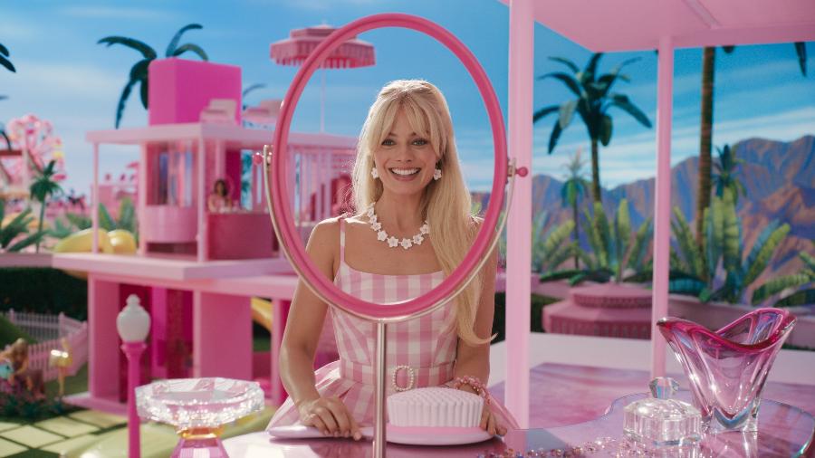 imagem do filme da Barbie, com a protagonista em um mundo rosa em frente a uma moldura de espelho