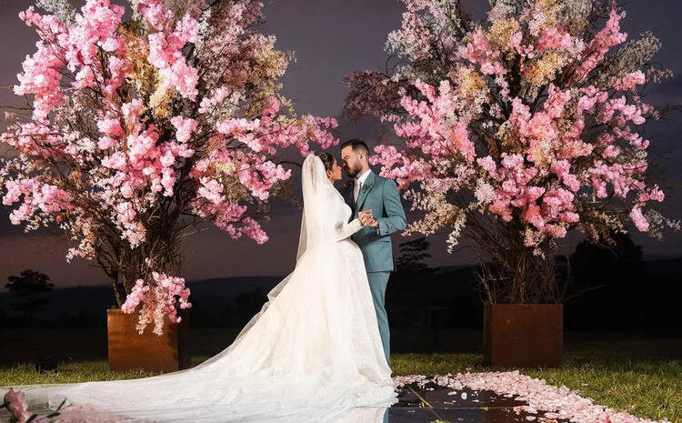 foto oficial do casamento de Maíra Cardi e Thiago Niro, com os dois se beijando ao lado de arranjos de flores cor de rosa