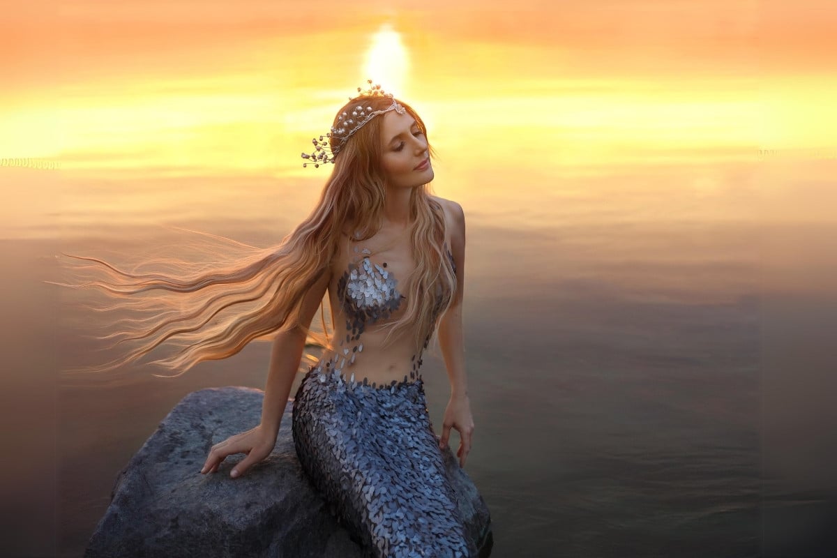 Mulher vestida de sereia em pedra com fundo de mar ao por do sol