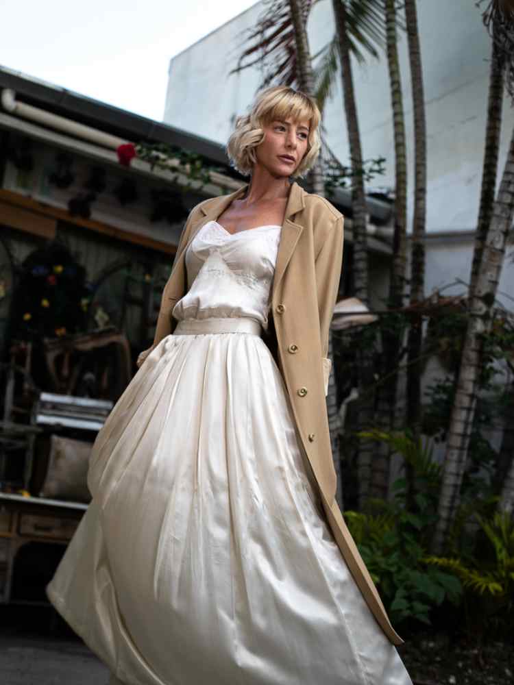 Mulher não-modelo com mais de 50 anos em ensaio fotográfico, usando vestido estilo de noiva, com blazer bege