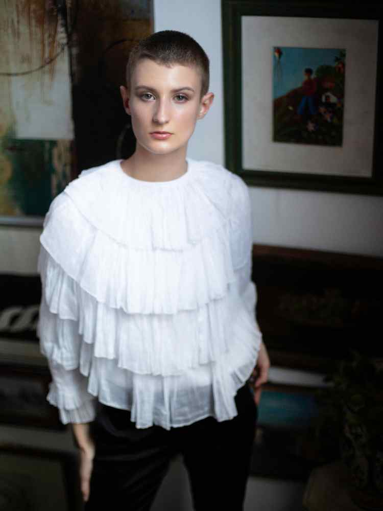 Mulher não-modelo com mais de 30 anos em ensaio fotográfico, usando blusa de babados branca + calça preta 