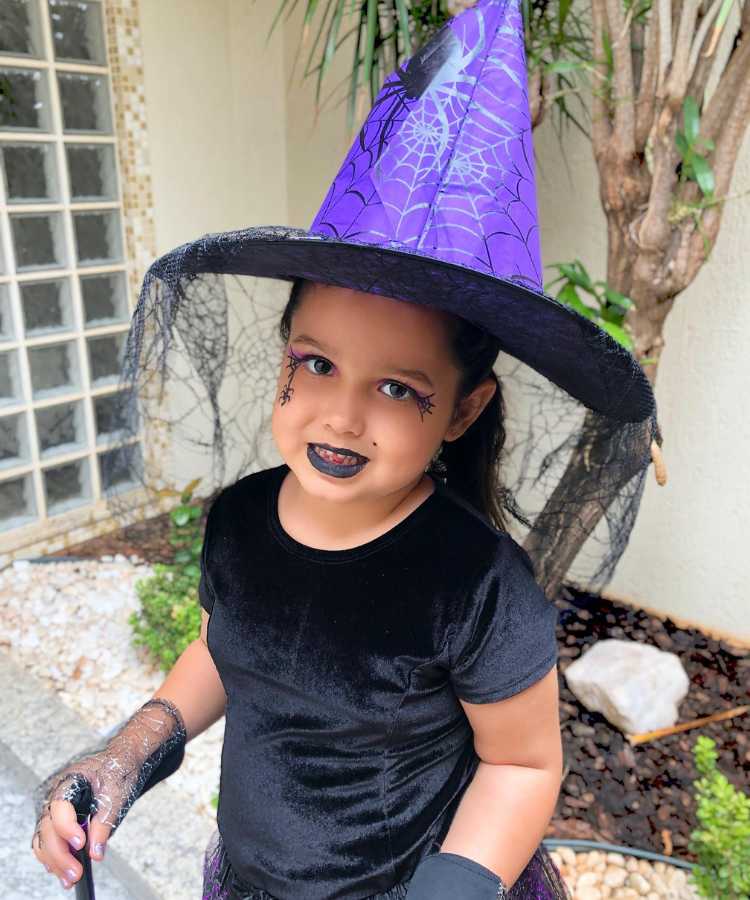 Garota maquaida de bruxa para o Halloween: Cores predominantes: preto e roxo. Usa: batom, sombra e delineado de aranha
