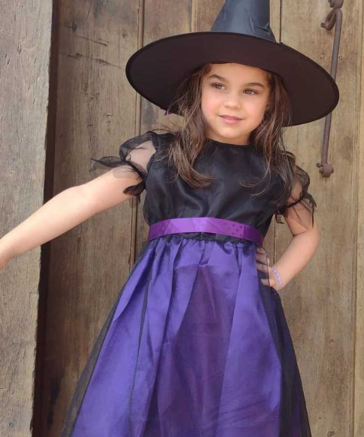 Garota fantasiada para o Halloween: Cores predominantes: preto e roxo. Usa: vestido e chapéu pontudo