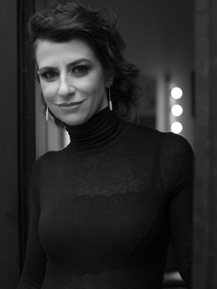 Mulher não-modelo com mais de 40 anos em ensaio fotográfico, usando blusa preta transparente com top de renda por baixo e acessórios elegantes
