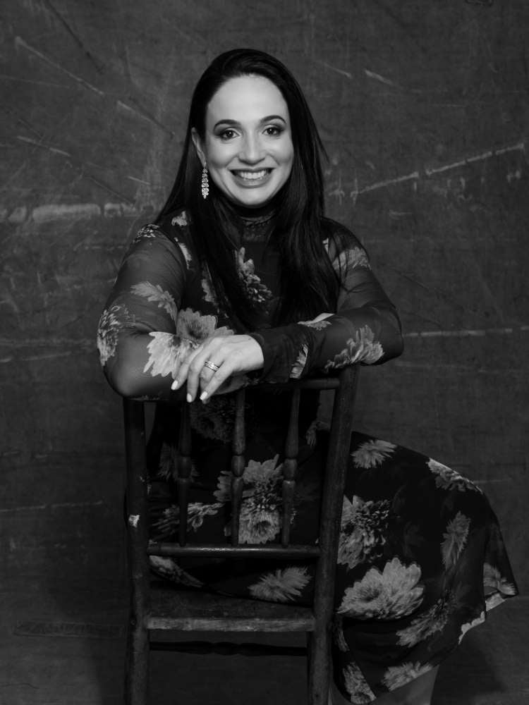 Mulher não-modelo com mais de 30 anos em ensaio fotográfico, usando vestido de floral, sentada em cadeira. Foto preto e branco