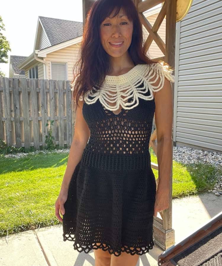 Mulher usando vestido preto de crochê e colar de crochê branco em formato de teia de aranha