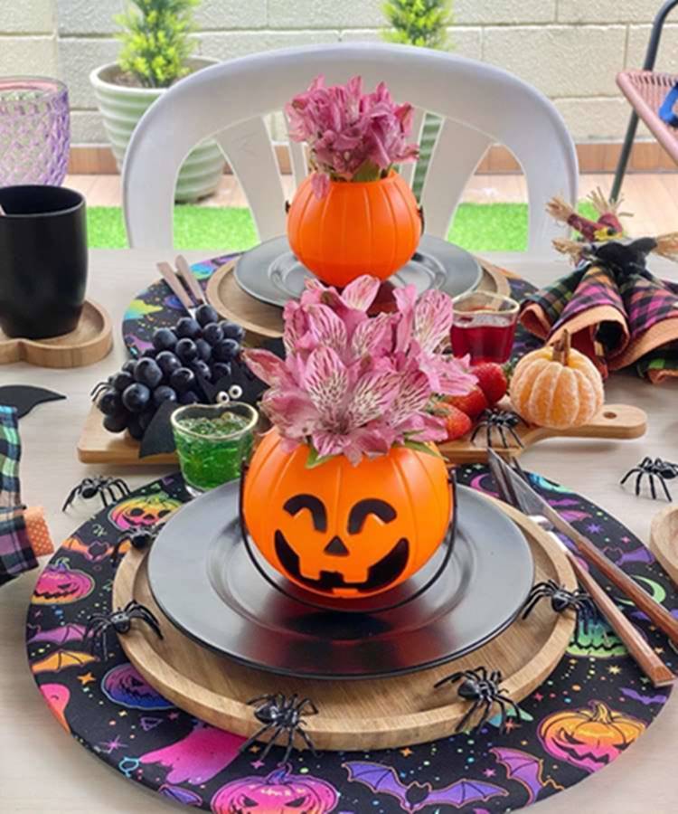 Mesa decorada de Halloween: baldinho de abóbora com flores em prato rodeado de aranhas falsas. Pocã descascada com galho pequeno