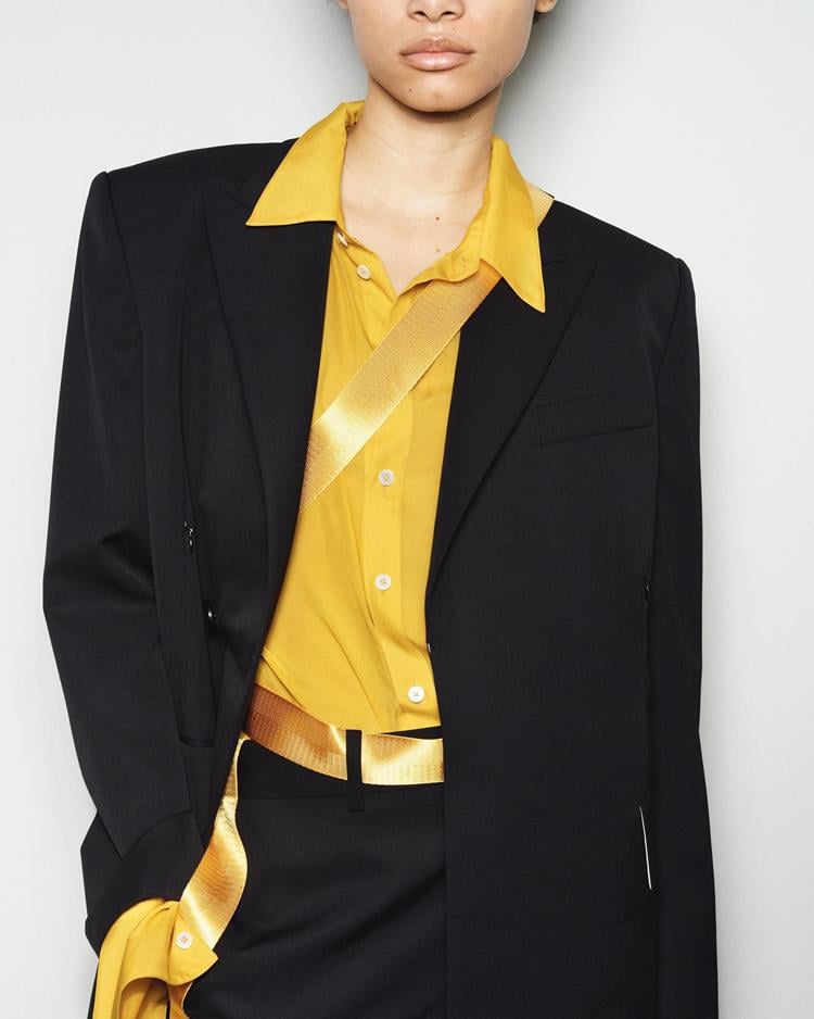 modelo com blazer e calça preta, camisa amarela por dentro