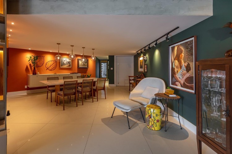 Foto ampla de sala de jantar com parede terracota, mesa grande e outra parede verde musgo com poltrona branca