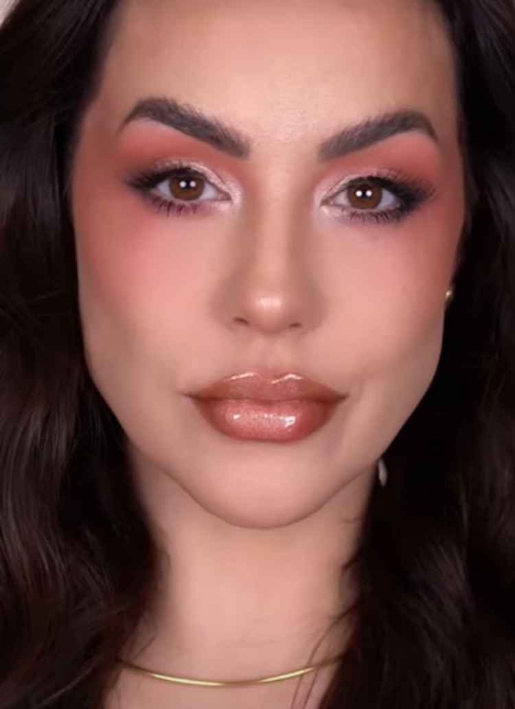 mulher de pele claro e cabelo escuro longo com maquiagem de tons fortes, blush e sombra rosados, os lábios em tom nude com efeito diamond