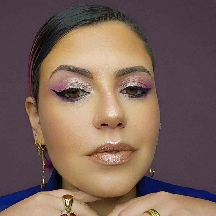 mulher de pele média, cabelo escuro preso e maquiagem em tons de roxo nos olhos e diamond lips