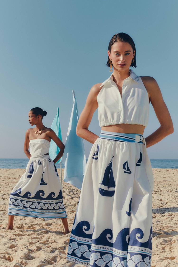 duas mulheres na praia com conjunto de top branco e saia de mesma cor com estampas náuticas azuis