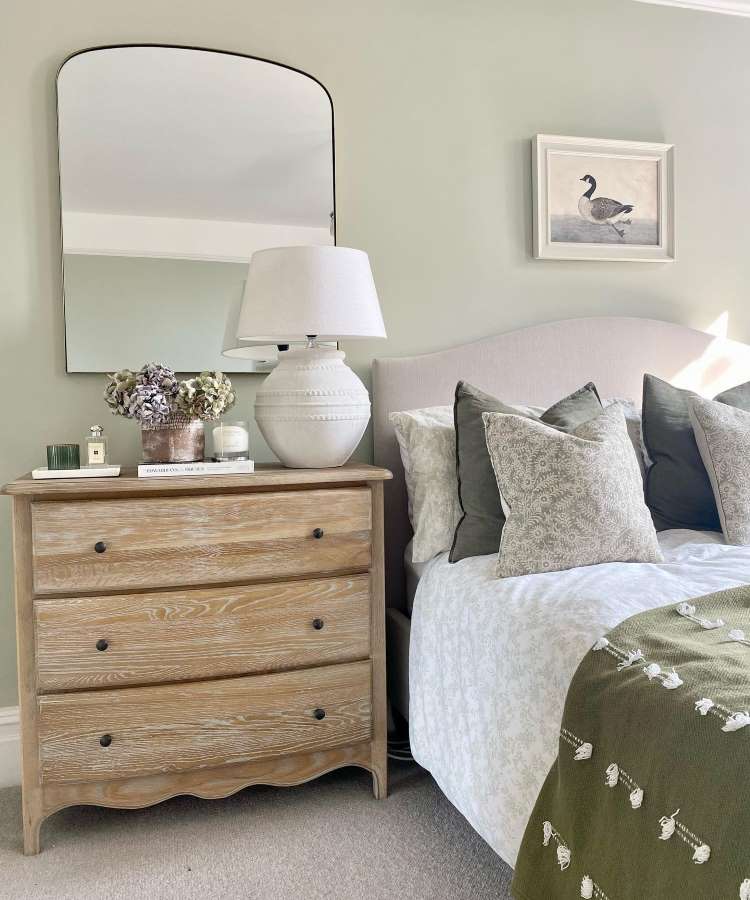 Elemento reflexivo quadrado no ambiente, pendurado na parede, em cima de cômoda. Cores predominantes: madeira clara, verde e cinza