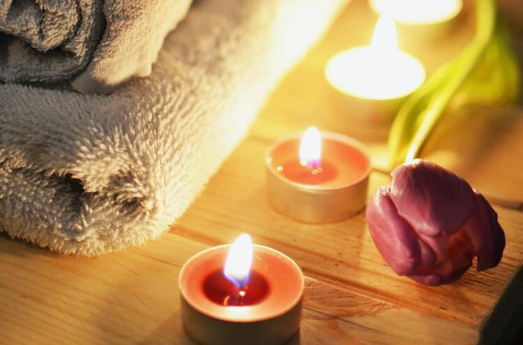 toalha de banho dobrada com uma rosa e velas pequenas acesas do lado