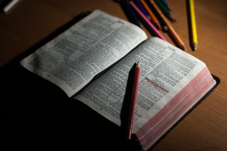 bíblia aberta com um lápis vermelho e alguns trechos grifados