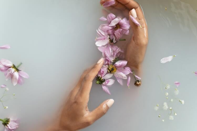 mãos femininas segurando flores em uma banheira com água leitosa
