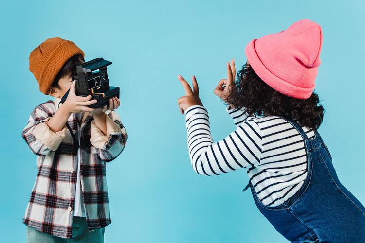 duas crianças, uma fotografando a outra com uma câmera analógica
