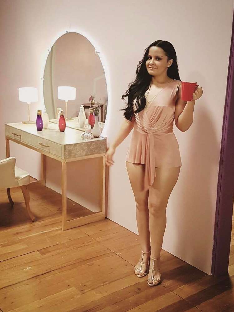 Foto de Maraisa em 2017, usando roupa curta rosada, salto, em cômodo com penteadeira, e segurando uma caneca vermelha