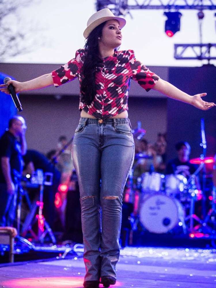 Maraisa em show de 2016, usando blusa estampada em vermelho, preto e branco, calça jeans de cós baixo e chapéu, segurando microfone com a banda atrás