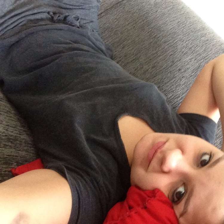 A cantora em selfie tirada em 2014, de blusa preta e sem sutiã, deitada em sofá com a cabeça apoiada em almofada vermelha