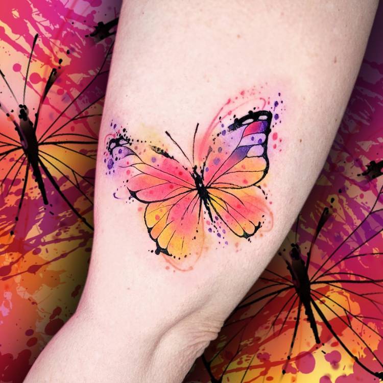 Tatuagem de uma borboleta em estilo aquarela com as cores roxo, rosa e amarelo. Ela está feita no braço de uma mulher de pele clara.