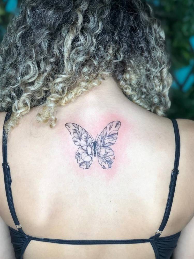 Tatuagem de borboleta nas costas de uma mulher de pele clara sendo as flores a estampa das asas.