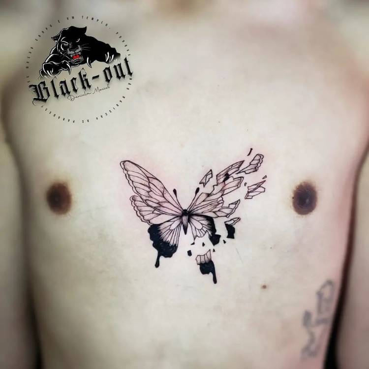Tatuagem de borboleta no peitoral de um homem de pele clara. A borboleta é em traços pretos, sombreados e sua asa direita está estilhaçada. 