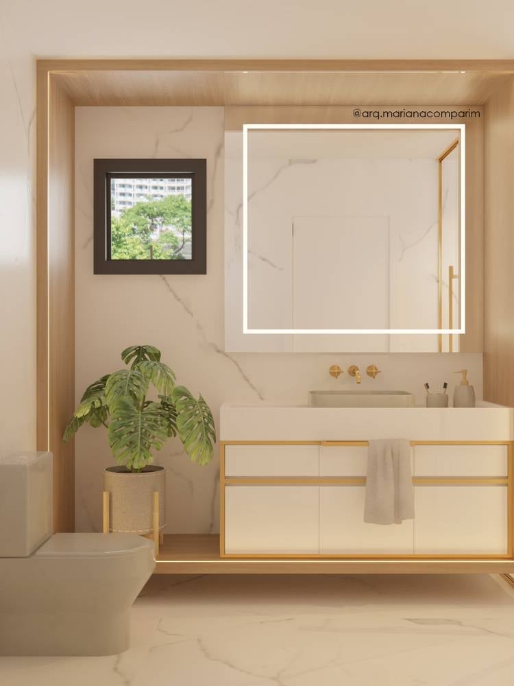 Parte de um banheiro com vaso sanitário à direita, vaso com costela-de-adão, janela acinma do vaso, pia e paredes marmorizadas e espelho quadrado com led. 