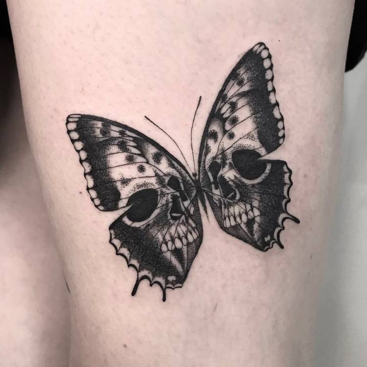 Tatuagem de borboleta com sombreamento e estampa de caveira, feita no braço de um homem de pele clara. 