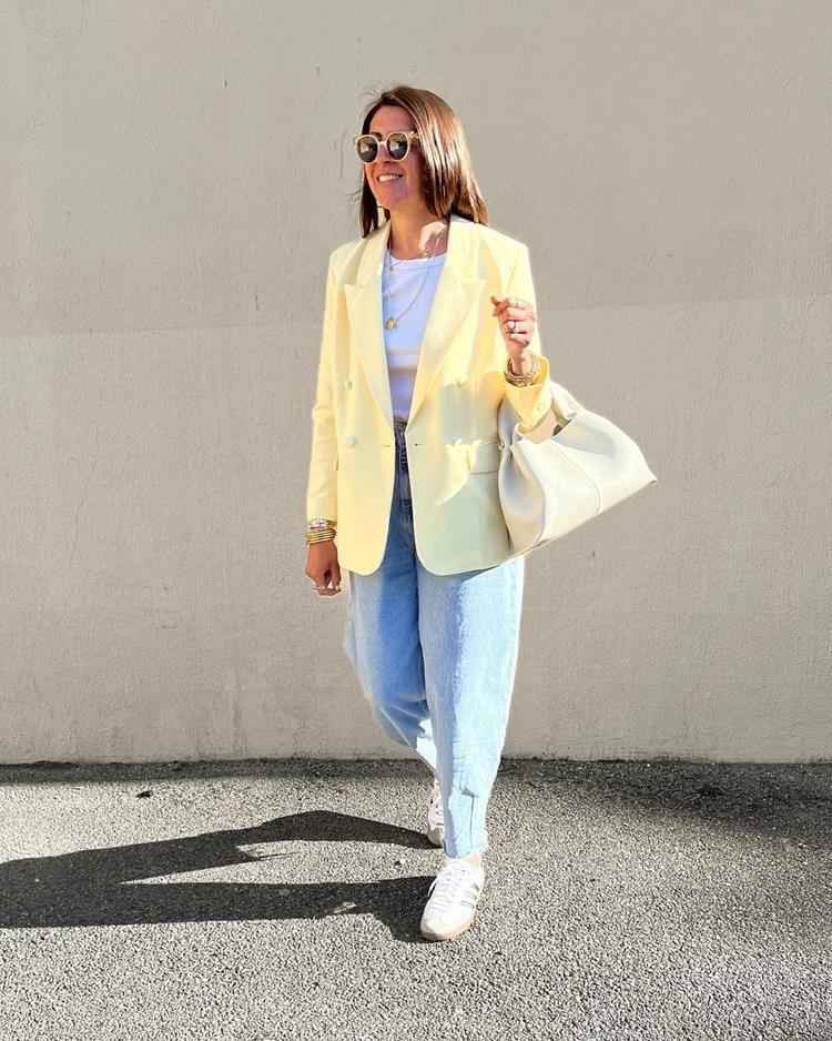 mulher com calça jeans, blusa branca e blazer amarelo por cima