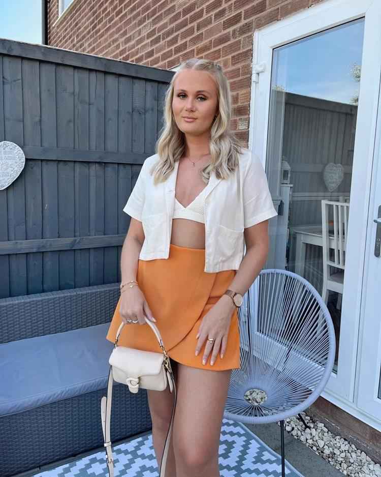 mulher com saia laranja, top e camisa branca