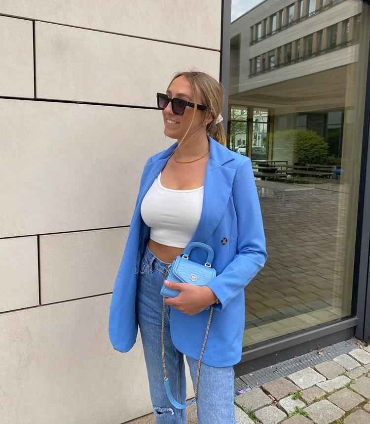 mulher com calça jeans, top branco e blazer azul