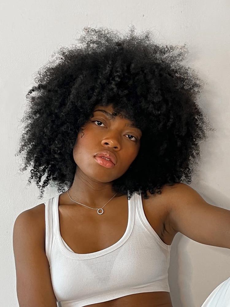Mulher com corte de cabelo afro fofo, uma das tendências do verão 2024. Ela tem o tom de pele escuro, usa cropped branco e tem o cabelo preto